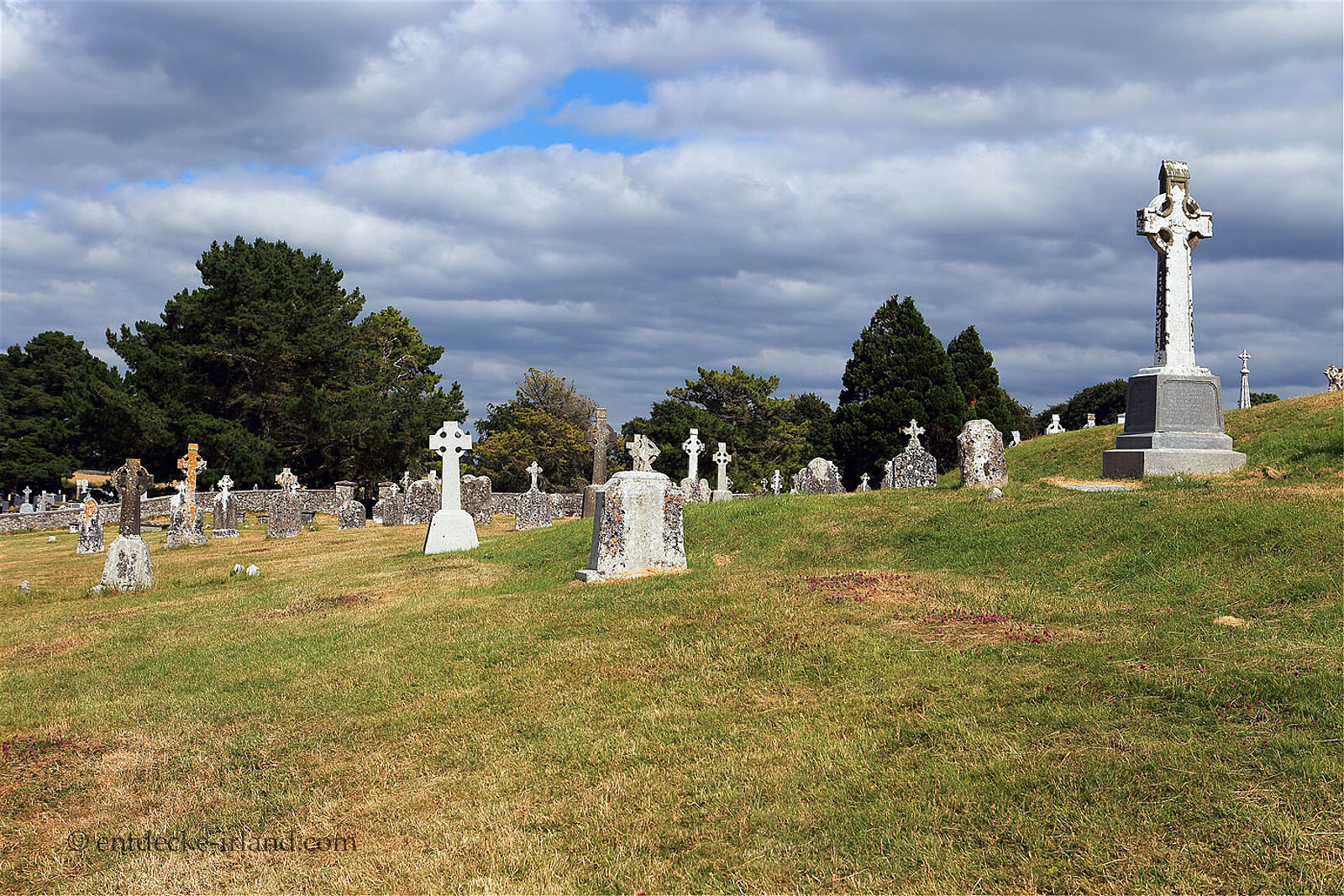 Kreuze auf dem Friedhof von Clonmacnoise im Sonnenlicht vor einem bewölkten Himmel